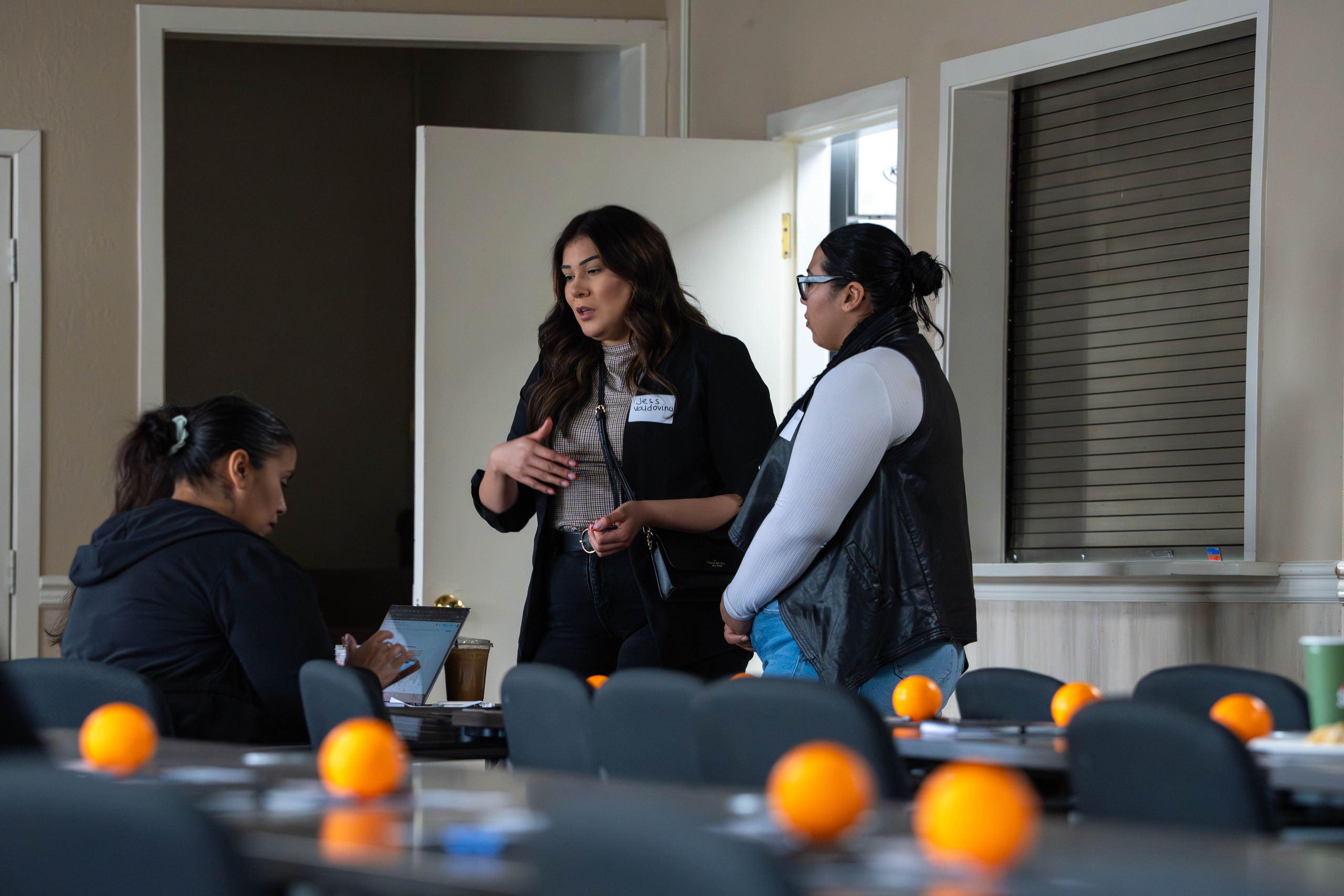 Workshop attendees talking between tables in the OIC of Washington training room, oranges on the tables in the foreground