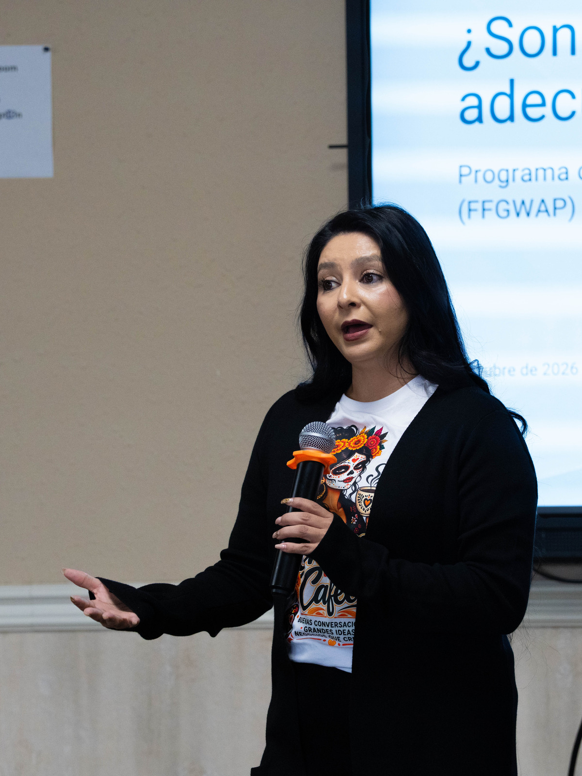A woman speaking into a microphone in front of a Spanish-language workshop slide